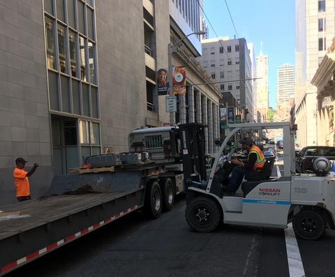 Reliable Crane delivers equipment on a busy city street and provides operator and forklift to move it indoors