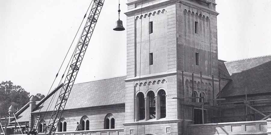1940s B&W photo of crane lifting bell into brick church tower