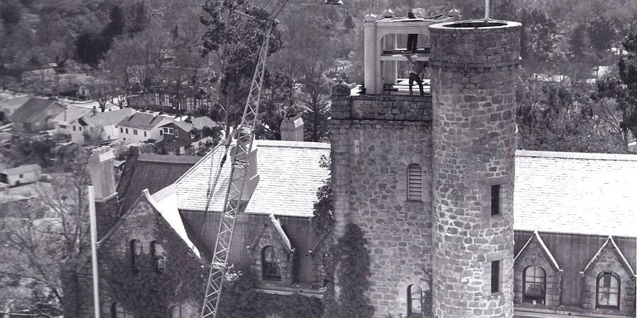 1940s B&W photo of crane lifting bell into old stone church tower